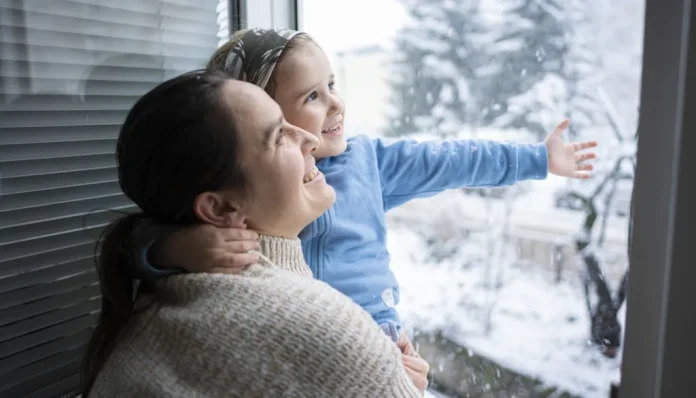 szellőzetés télen anya és kislánya állnak mosolyogva a nyitott ablaknál