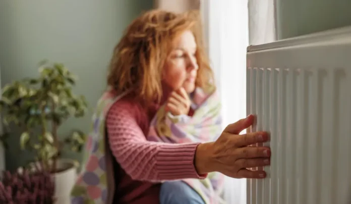 A hideg radiátort fogja egy nő otthon fázik