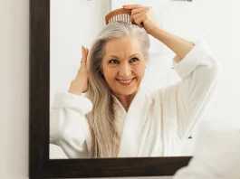 Mosolygó idős nő fésülködik fürdőszobai tükör előtt